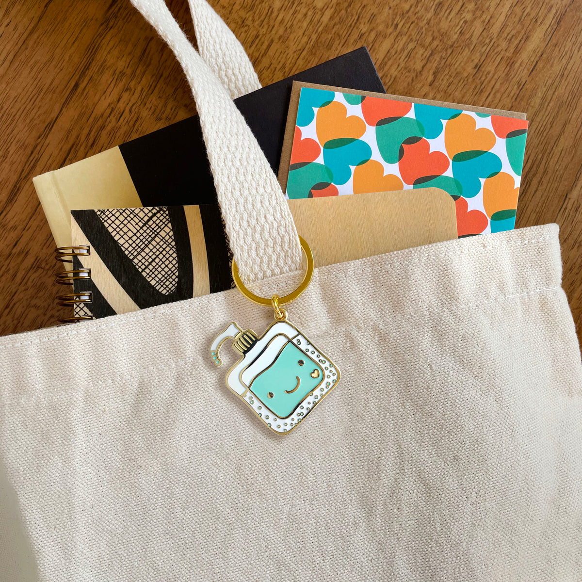 Happy Hand Sanitizer enamel keychain hanging from a tote bag handle