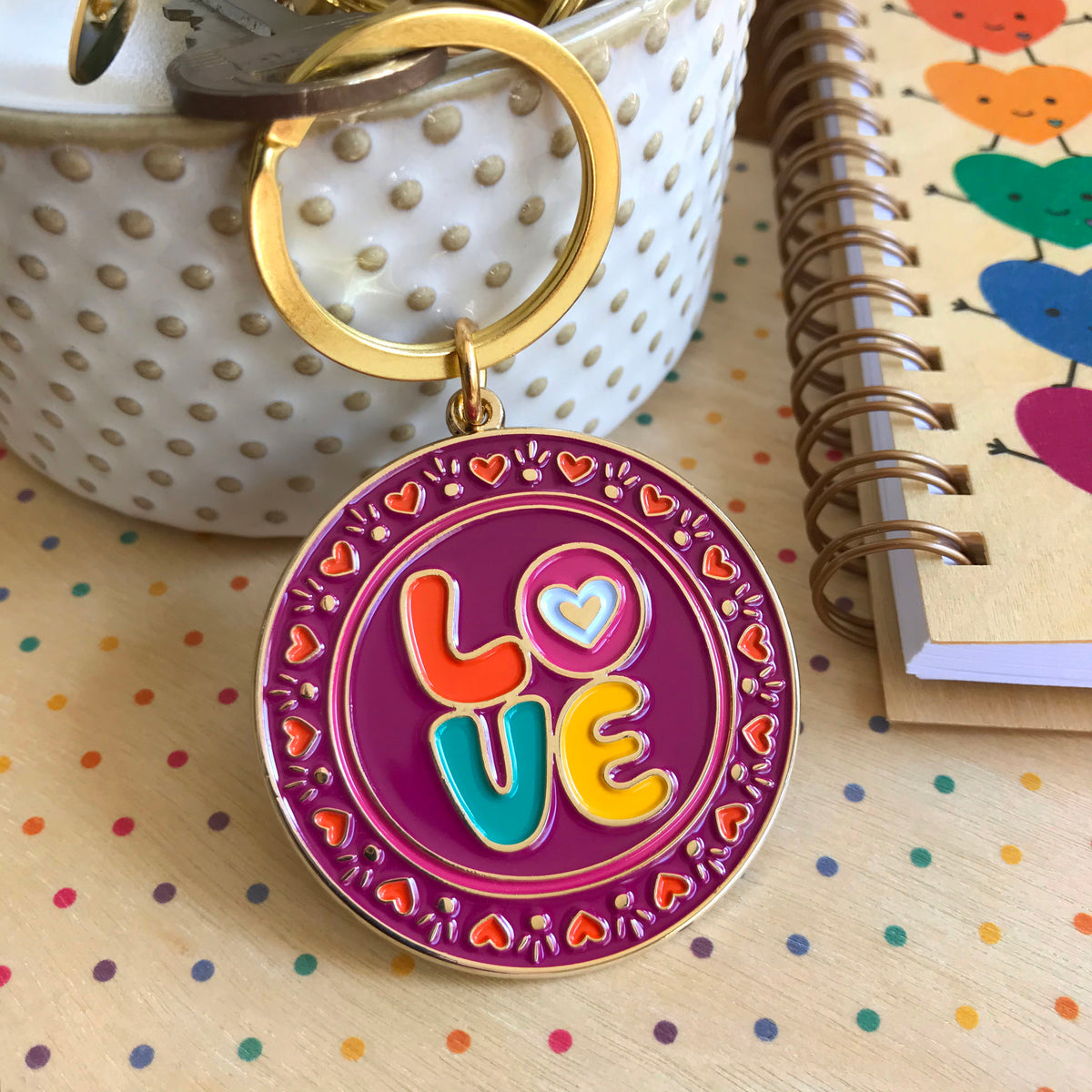 Gold metal Love enamel keychain featuring a colorful "LOVE" design with heart details on a magenta round background on a gold key ring