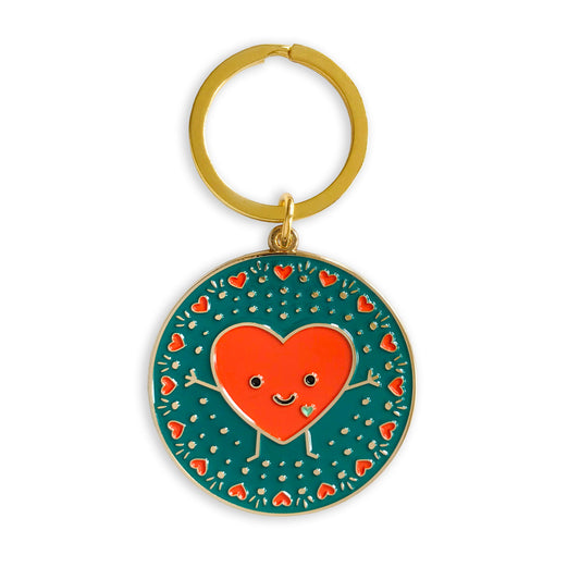Gold metal keychain with a smiling red heart design on a teal background bordered with small red hearts.