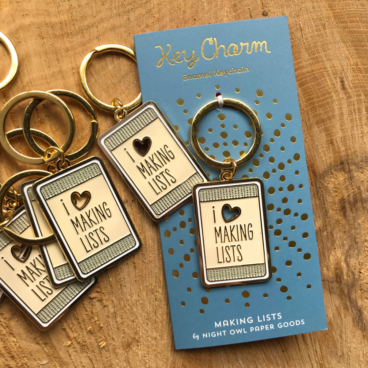 Making Lists enamel keychain on gold foil stamped backer card, alongside additional Making Lists enamel keychains. Soft blue backer card reads "Key Charm Enamel Keychain" at top and "Making Lists by Night Owl Paper Goods" at bottom.