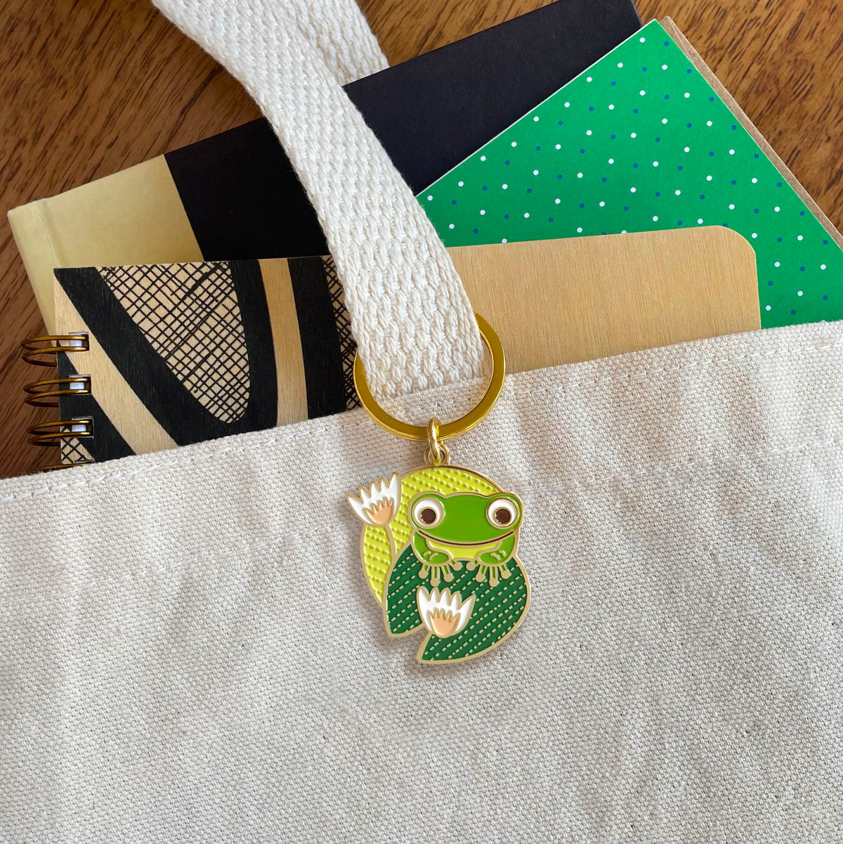 Frog enamel keychain hanging from a canvas tote bag handle