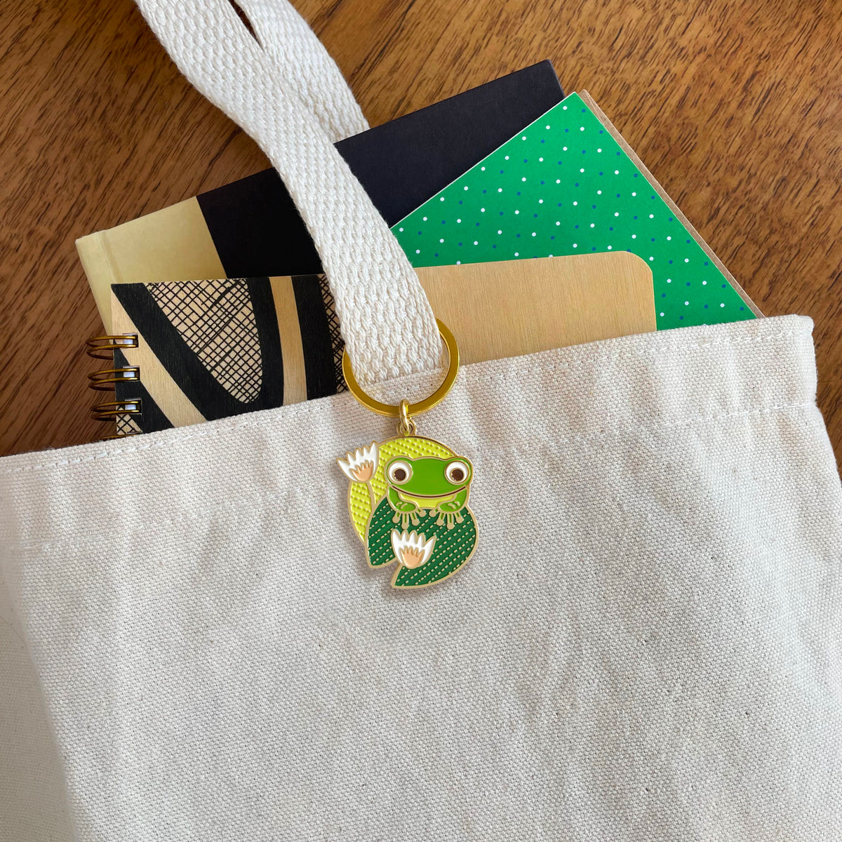 Frog enamel keychain hanging from a canvas tote bag handle