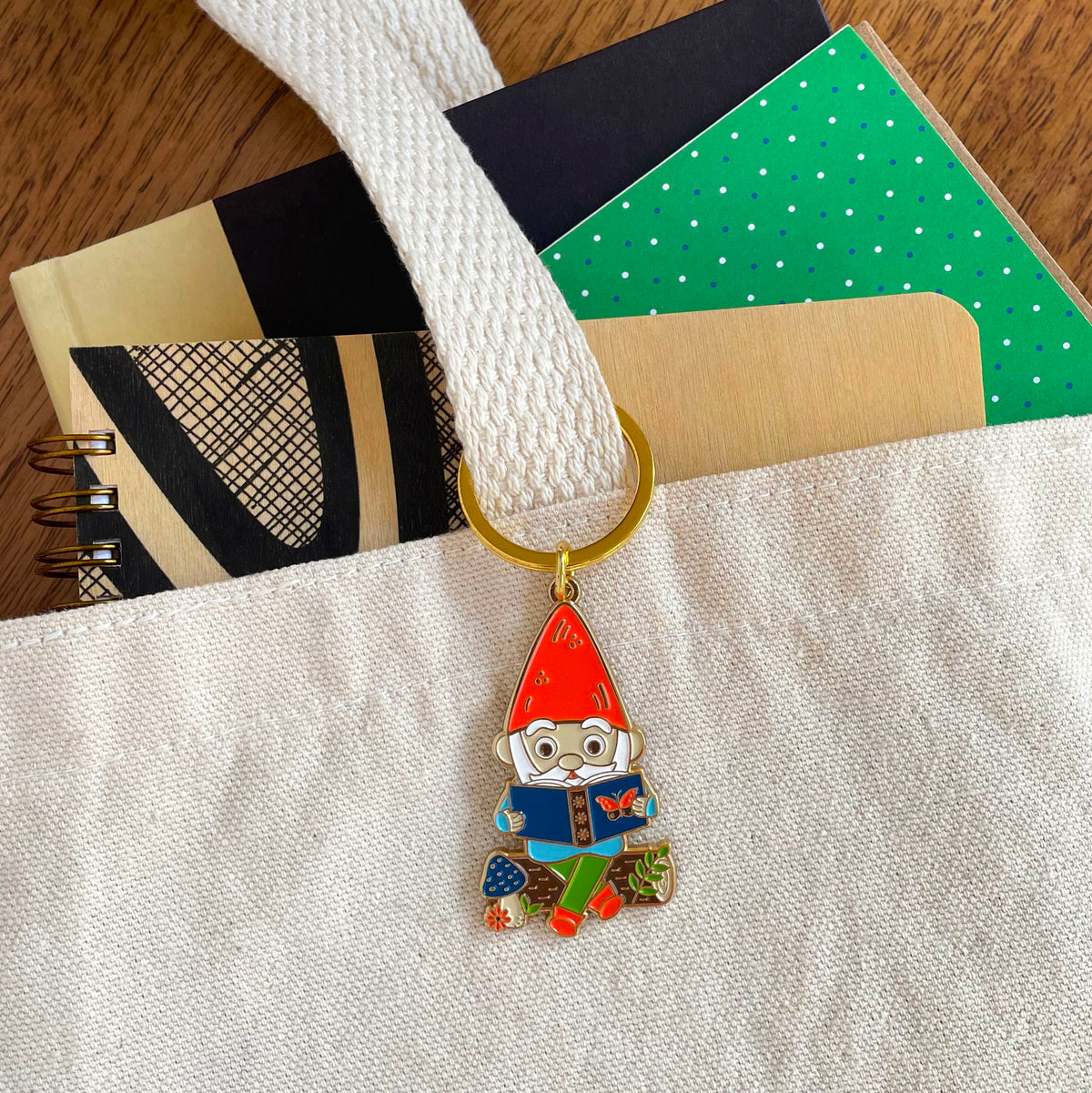 Reading Gnome enamel keychain hanging from a canvas tote bag handle