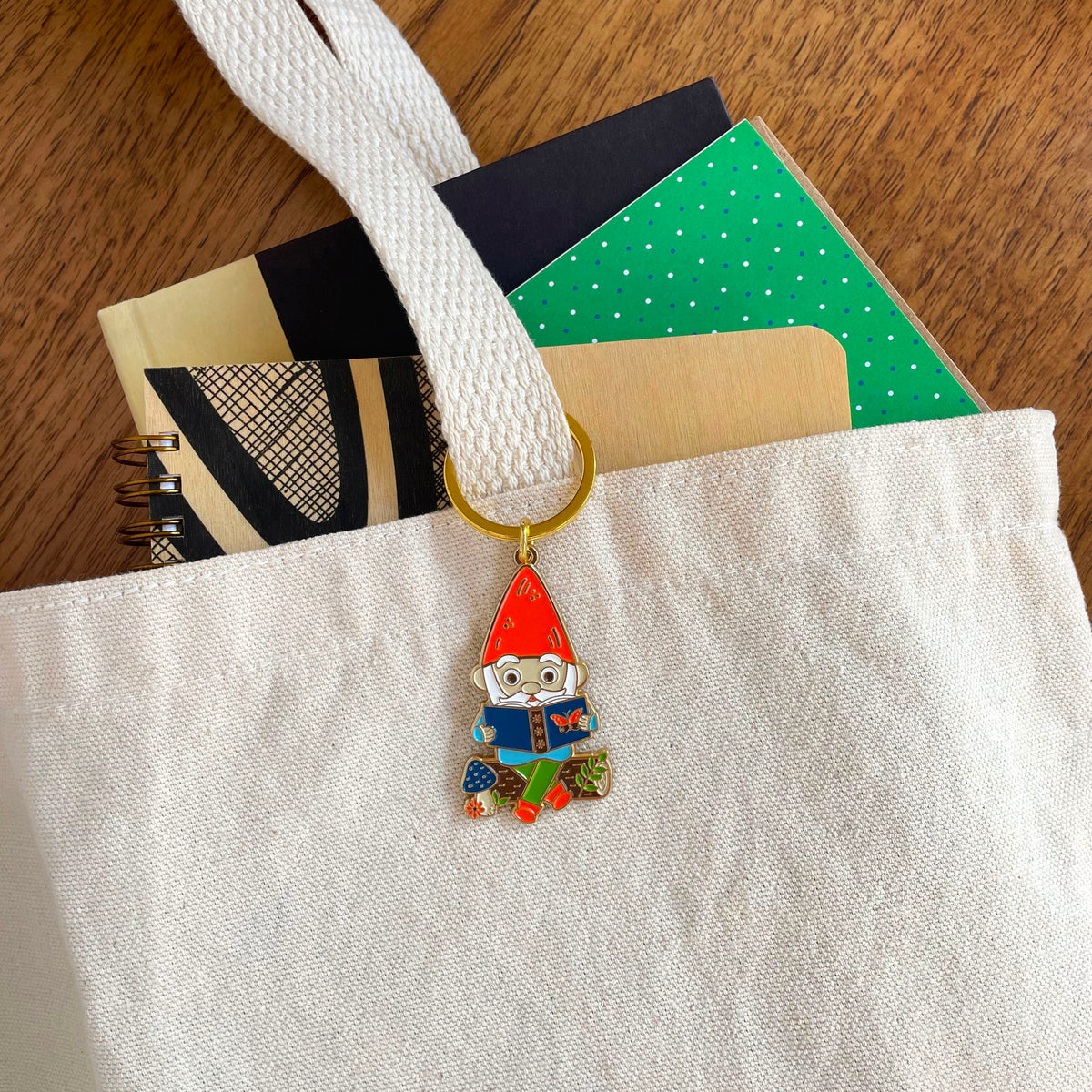 Reading Gnome enamel keychain hanging from a canvas tote bag handle