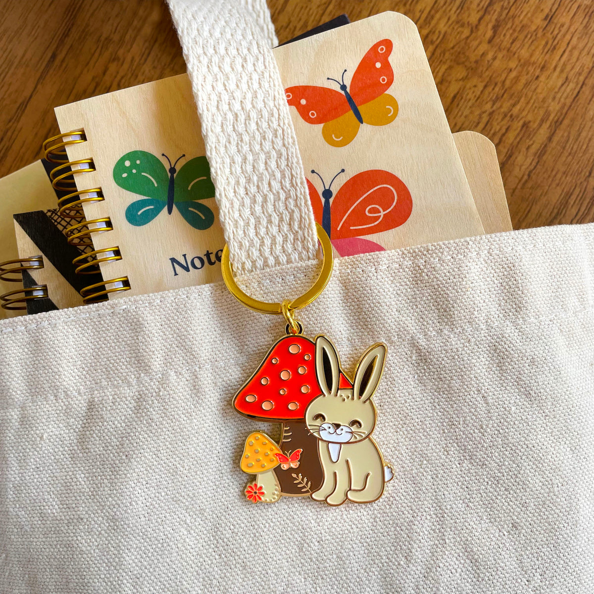 Bunny Rabbit keychain hanging from a canvas tote bag with a butterfly-themed notebook in the background.