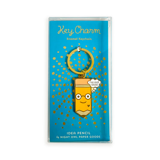 Idea Pencil enamel keychain on gold foil stamped teal backer card packaged in a clear gift box. Backer card reads "Key Charm Enamel Keychain" at top and "Idea Pencil by Night Owl Paper Goods" at bottom.

