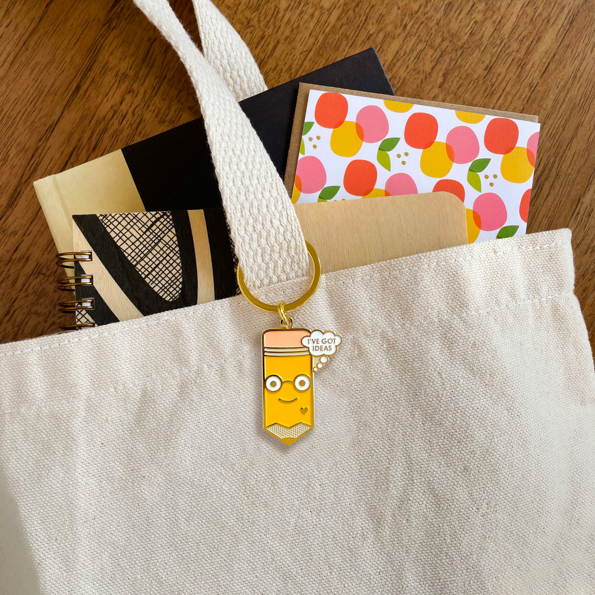 Idea Pencil enamel keychain hanging from a canvas tote bag handle