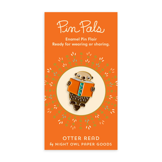 Enamel pin of an otter reading a book mounted on an orange backer card