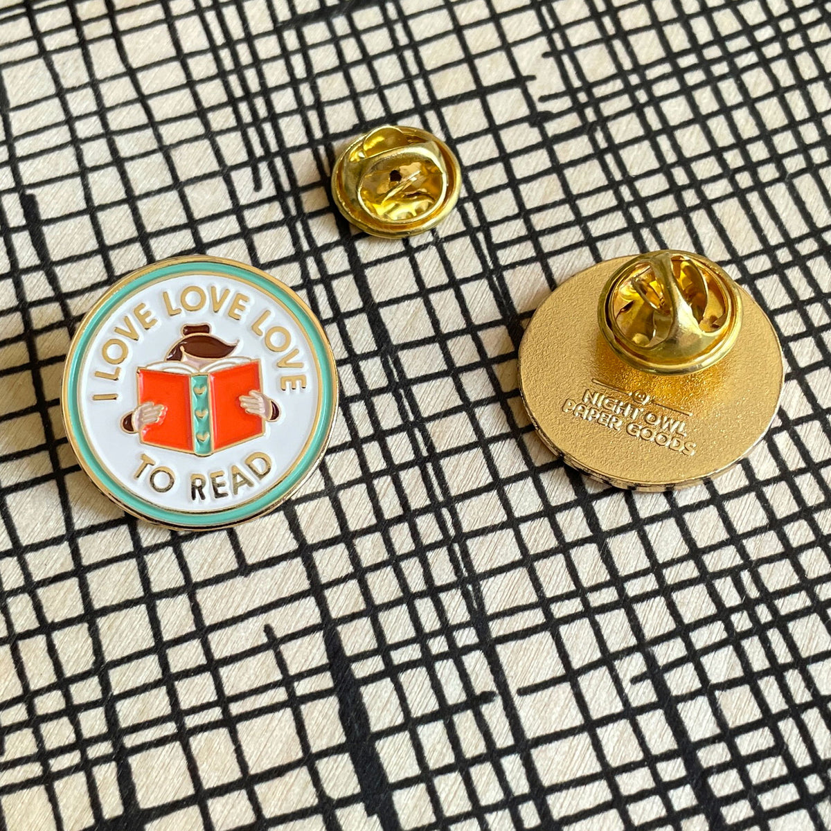 Front and back view of Love to Read enamel pin. Front shows a woman with an open book and "I Love Love Love to Read" text and back is gold with the Night Owl Paper Goods logo and butterfly clasp.