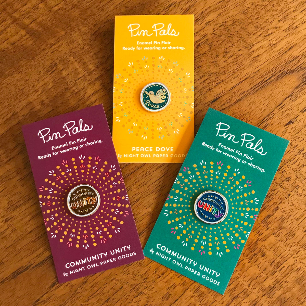 Community Unity Tones, Peace Dove and Community Unity Colors enamel pins on their backer cards, all pictured together.