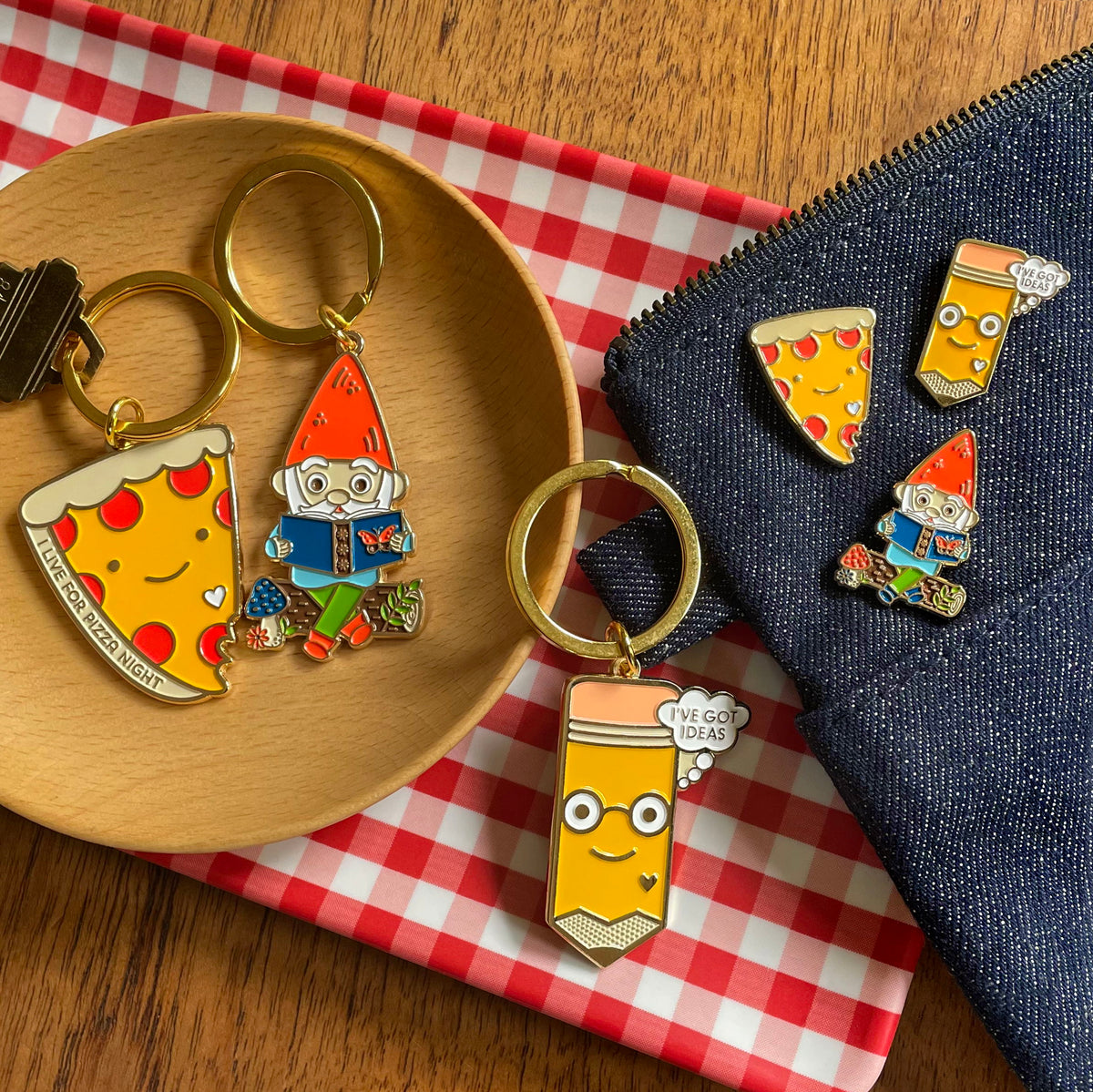 Group of cute flat ring keychains: Reading Gnome with red hat and green pants sitting on a log, Pizza with pepperoni and text 'I live for Pizza Night' and yellow pencil with smiling face and eye glasses with text 'I've Got Ideas'.