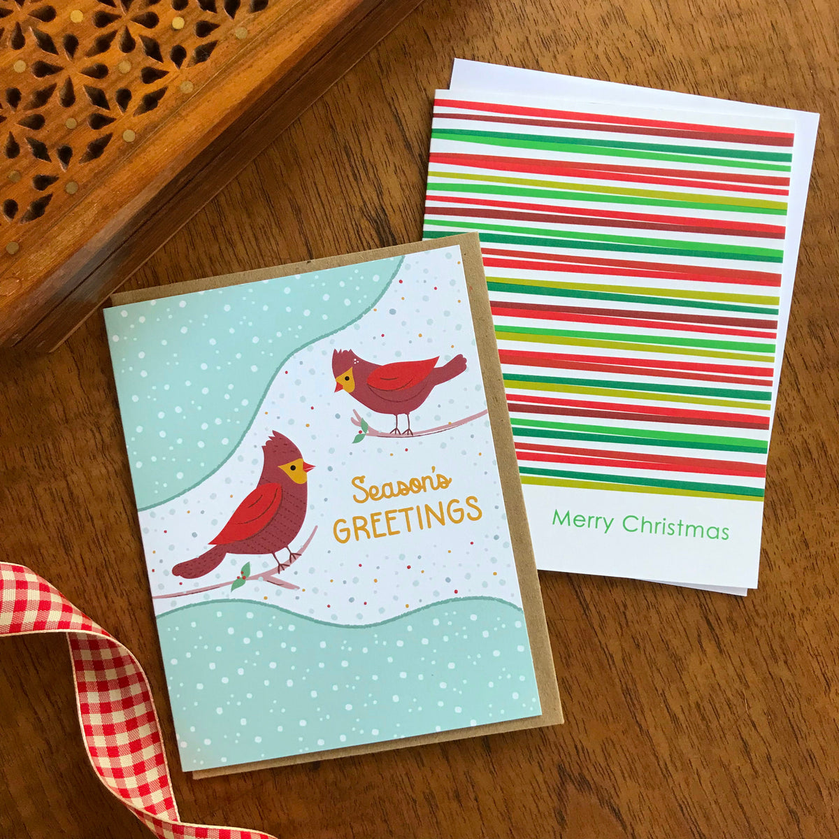 Cardinal Greetings and Simply Merry holiday cards shown side by side on a wood tabletop.