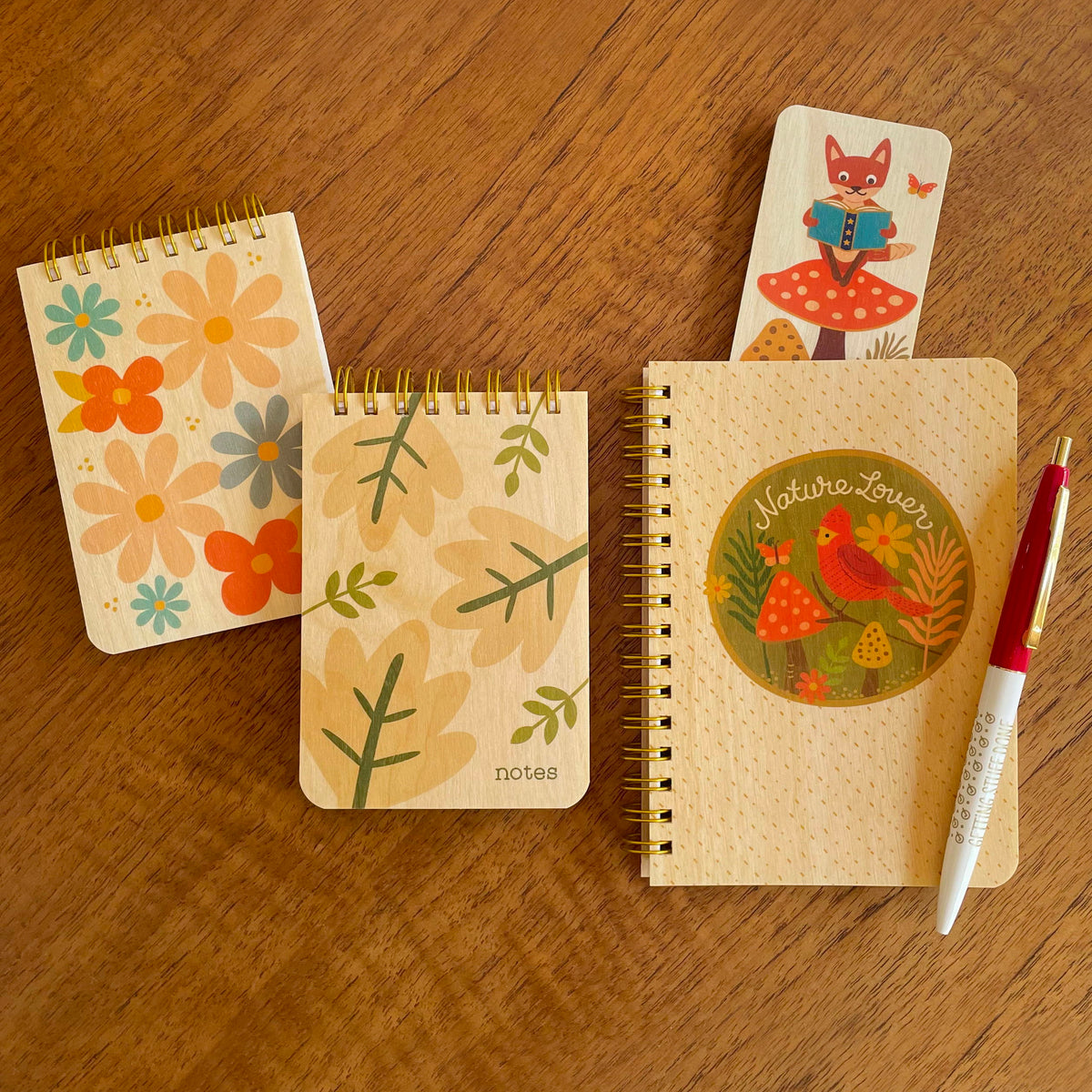 Nature Lover notebook featuring a red bird and forest scene, two mini notepads with wood covers featuring colorful flowers and leaves, a Reading Fox bookmark and a ballpoint pen.