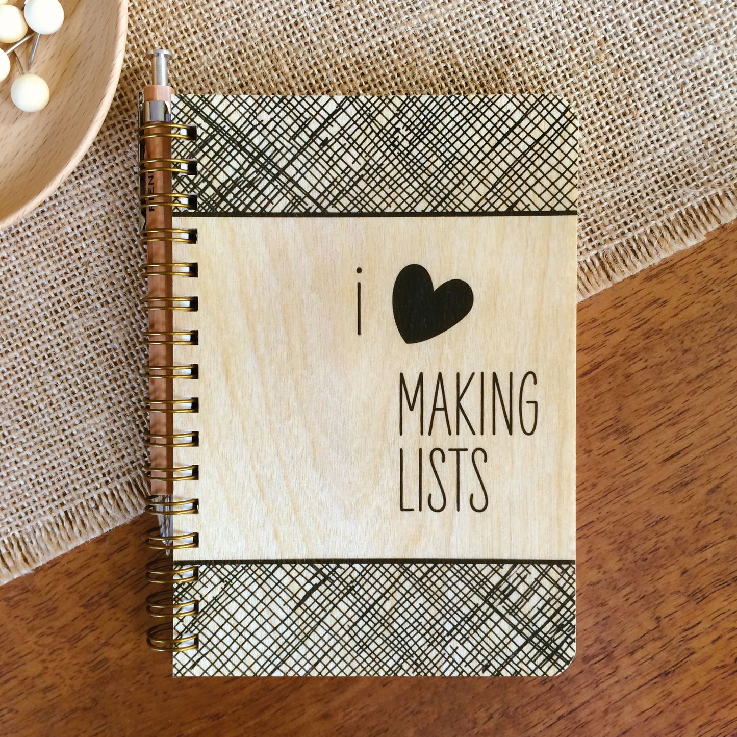 Spiral-bound wood notebook with birch wood covers featuring "I ♥ Making Lists" text and a black crosshatch border sitting on a wood table.