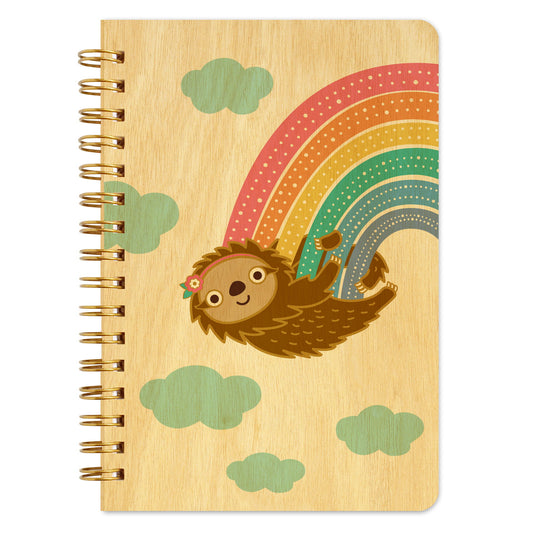 Spiral-bound wood notebook with birch wood covers featuring a sloth with a floral headband hanging from a rainbow among clouds.