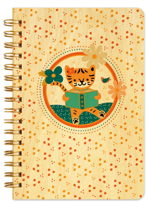 Spiral-bound wood notebook with birch wood covers featuring an orange striped cat reading a book inside a circular frame with flowers and a small bird on a speckled orange background.