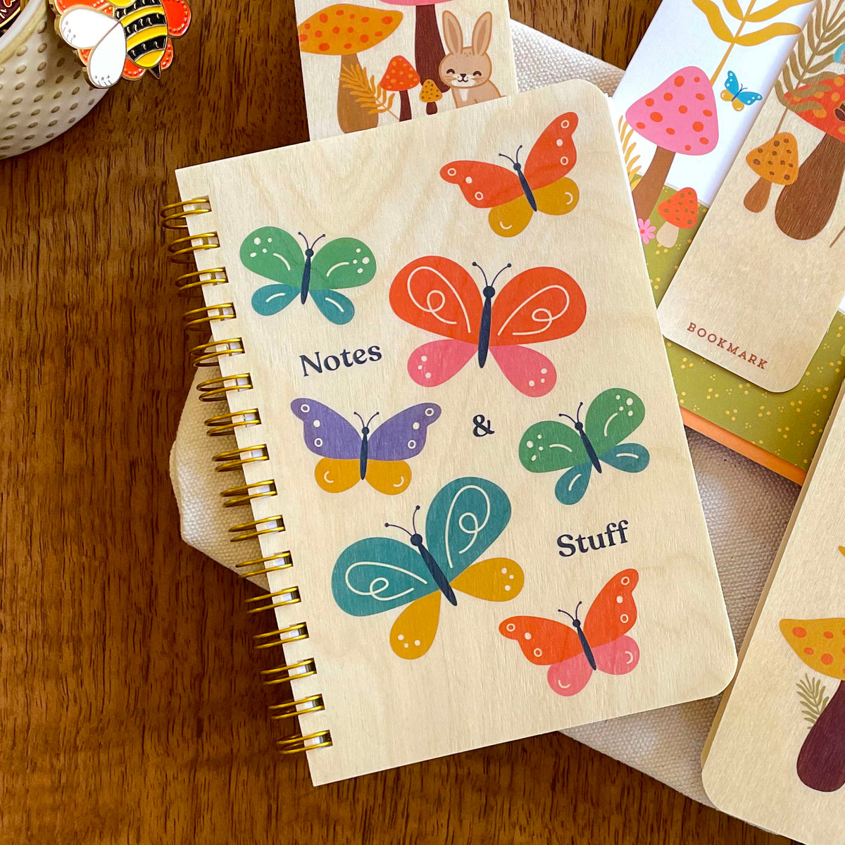 Spiral-bound wood notebook with birch wood covers featuring colorful butterflies in green, orange, teal and purple with "Notes & Stuff" text.