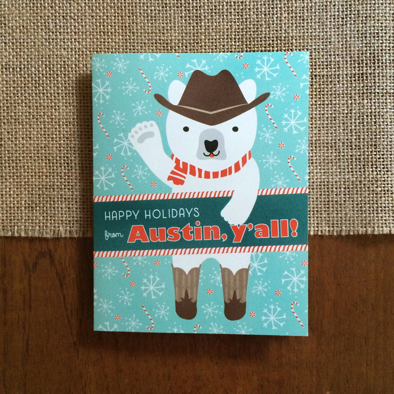 Polar Austin folded paper holiday card featuring a polar bear in a cowboy hat, red striped scarf and cowboy boots waving against a teal background with snowflakes and candy canes and the greeting "Happy Holidays from Austin, y'all!"