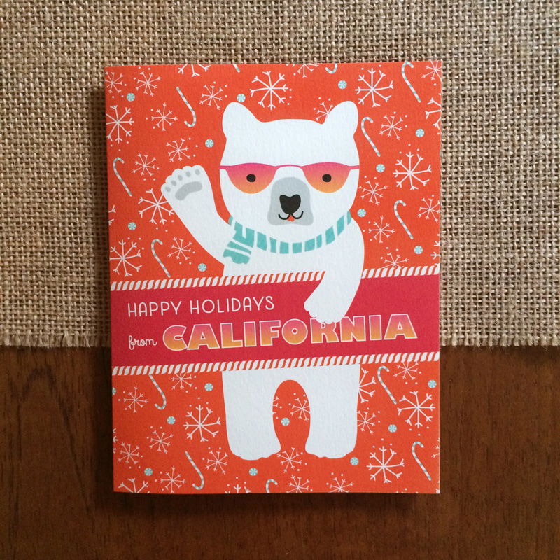 Polar California folded paper holiday card featuring a polar bear in pink sunglasses and an aqua scarf waving against a bright orange background with snowflakes and candy canes and the greeting "Happy Holidays from California"