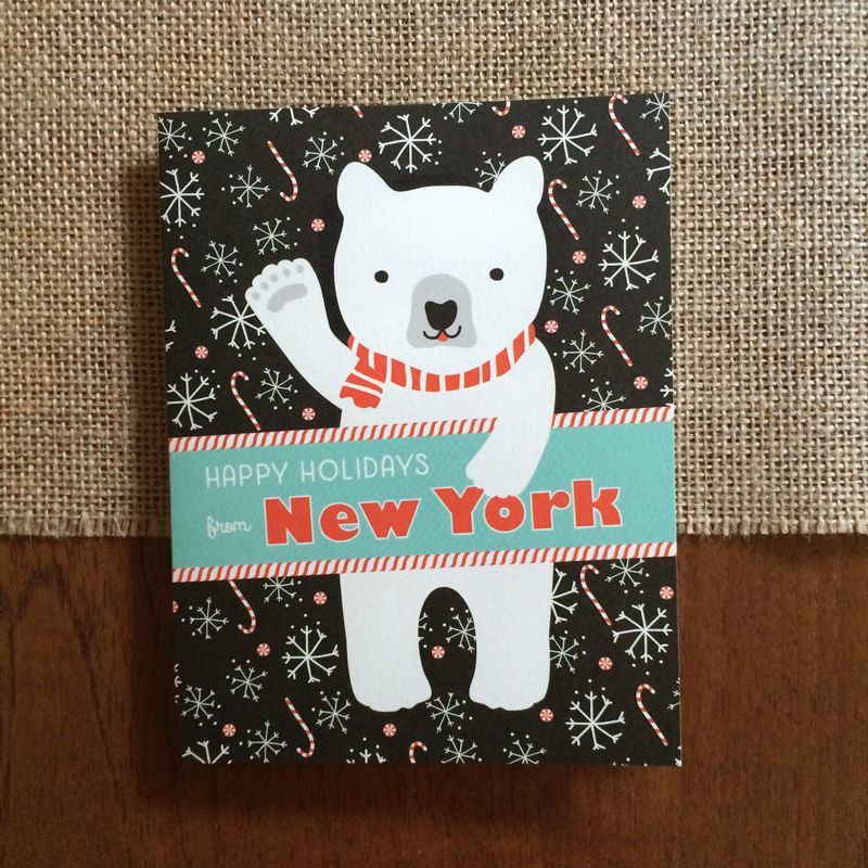 Polar New York folded paper holiday card featuring a polar bear in a red striped scarf waving against a black background with snowflakes and candy canes and the greeting "Happy Holidays from New York"
