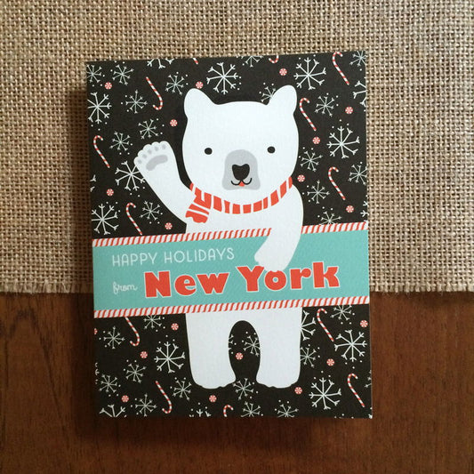 Polar New York folded paper holiday card featuring a polar bear in a red striped scarf waving against a black background with snowflakes and candy canes and the greeting "Happy Holidays from New York"