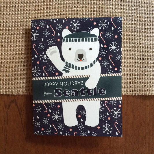 Polar Seattle folded paper holiday card featuring a polar bear in a teal beanie and scarf waving against a navy blue background with snowflakes, raindrops and candy canes and the greeting "Happy Holidays from Seattle"