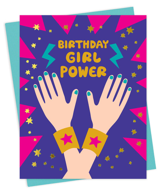 Front of colorful foil-stamped Birthday Girl Power birthday card with gold foil stars, pink burst background, lightning bolts and illustrated hands with teal nail polish raised in a celebratory pose. Shown with a light blue envelope.