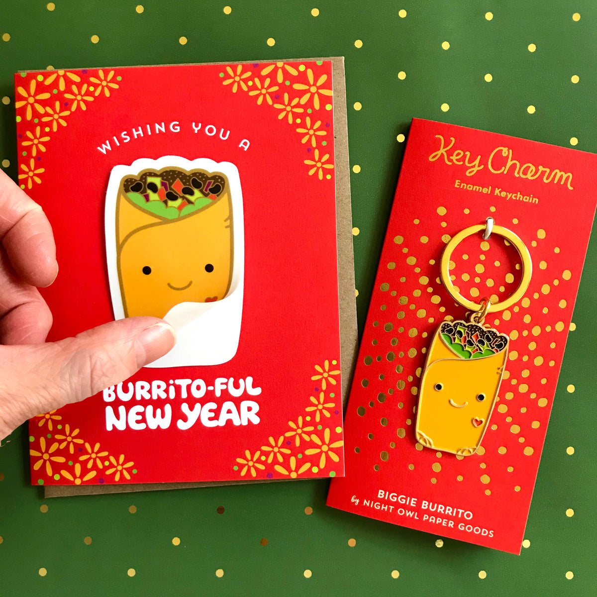 Burrito-Ful New Year Sticker card with dishwasher safe removable vinyl sticker alongside a Burrito Key Charm. Finger is lifting up the sticker to demonstrate that it's removable.