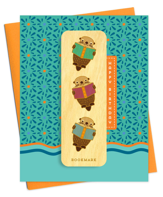 Folded birthday greeting card with a bold teal and orange pattern and wavy waterline design, Happy Birthday text and a removable birch wood bookmark featuring illustrated otters reading books. Pictured with an orange envelope.