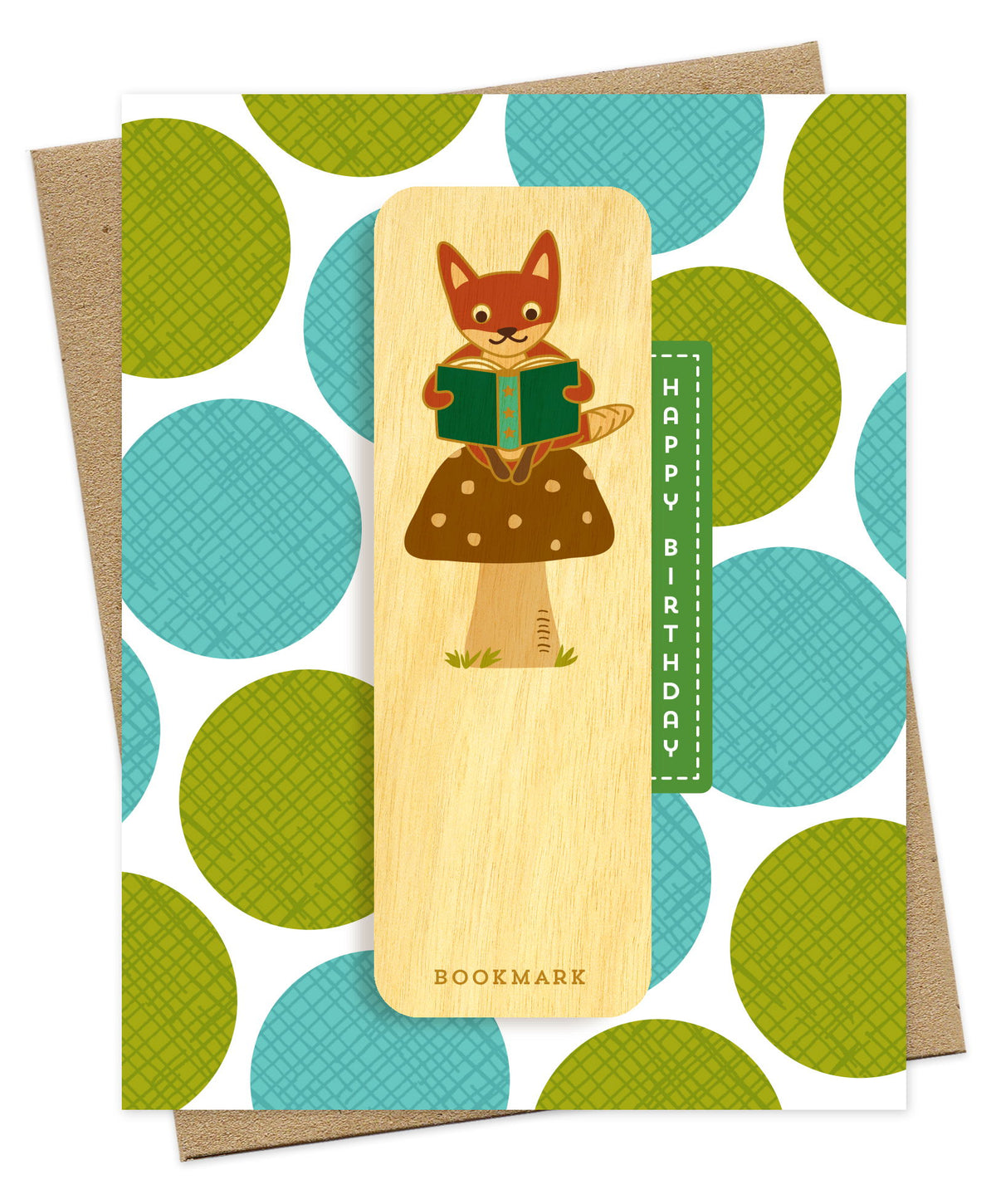 Folded birthday greeting card with a white background and oversized green and teal polka dot pattern, Happy Birthday text and a removable birch wood bookmark featuring a fox reading a book while perched on a mushroom. Pictured with a kraft envelope.