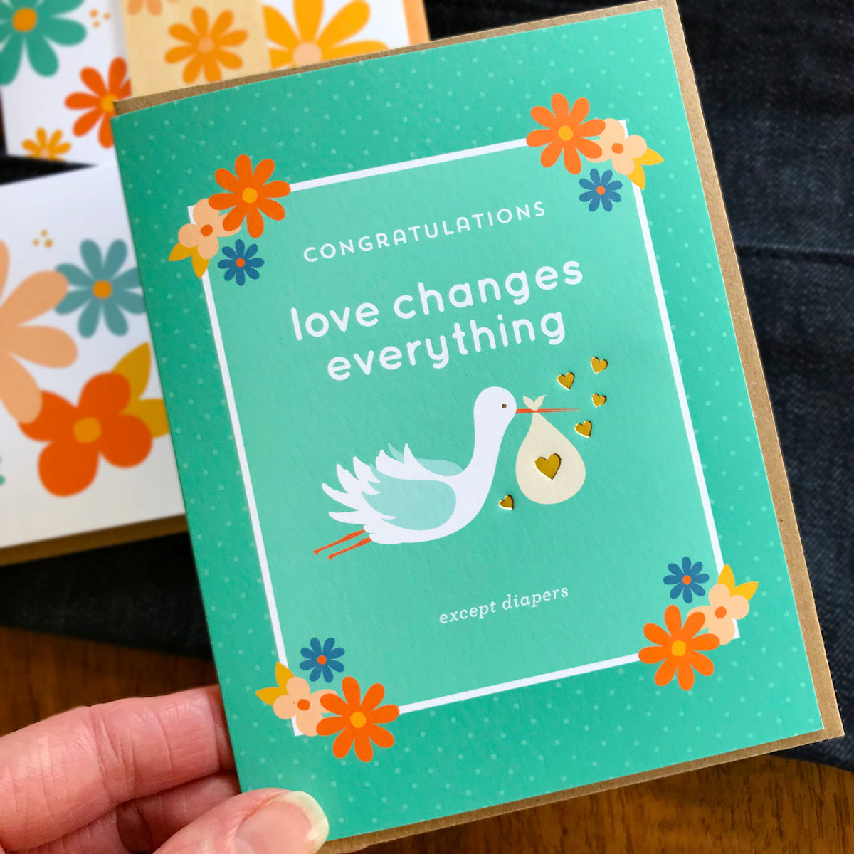 Baby shower card with stork and text 'Congratulations love changes everything except diapers' held by a hand.
