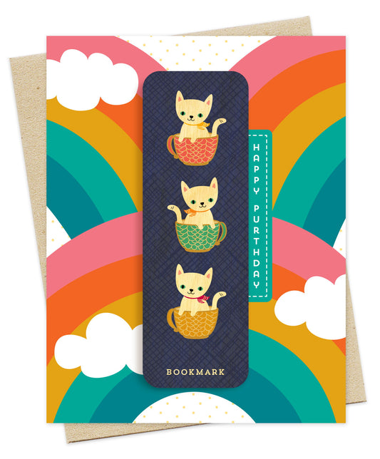 Folded birthday greeting card with a vibrant rainbow design, Happy Purthdday text and a removable birch wood bookmark featuring illustrated cats in teacups. Pictured with a kraft envelope.