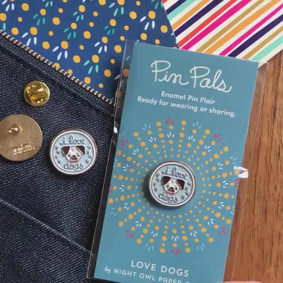 Front of enamel pin is a smiling dog and "I love dogs" text with gold accents. Back of pin is gold with the Night Owl Paper Goods script logo. Pin is mounted on a backer card that says "Pin Pals - Enamel Pin Flair - Ready for wearing or sharing - LOVE DOGS - by Night Owl Paper Goods" and is packaged in a clear bag.