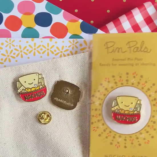 Front of enamel pin is a smiling bowl of nachos with gold accents. Back of pin is gold with the Night Owl Paper Goods script logo. Pin is mounted on a backer card that says "Pin Pals - Enamel Pin Flair - Ready for wearing or sharing - NACHO LOVER - by Night Owl Paper Goods" and is packaged in a clear bag.