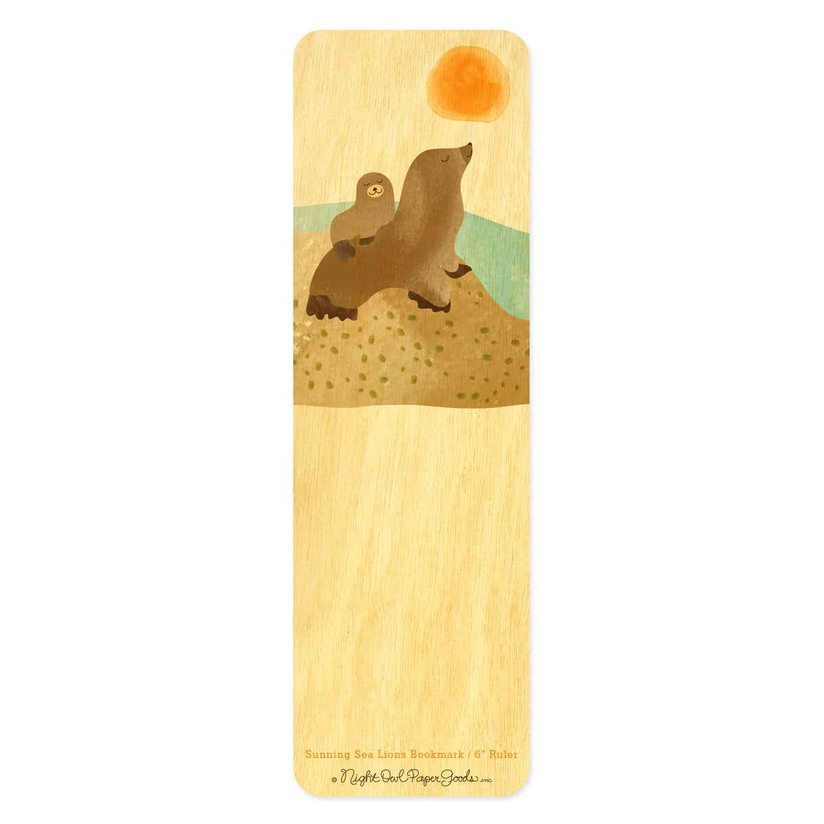 Birch wood bookmark with two content sea lions sitting on a rocky beach with sun and water in the background. Bottom text reads "Sunning Sea Lions Bookmark / 6" Ruler" followed by the Night Owl Paper Goods script logo.